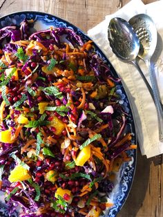 a salad with carrots, cabbage and other vegetables on a blue plate next to a spoon