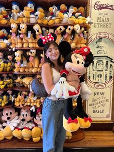 a woman holding a stuffed mickey mouse in front of a store filled with lots of stuffed animals