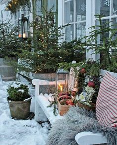 the porch is covered in snow and decorated with christmas trees, potted plants and candles