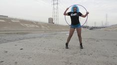 a woman holding a hula hoop while standing on top of a dirt field next to power lines