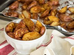 a white bowl filled with cooked potatoes next to a baking pan full of seasoned potatoes