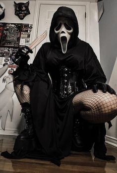 a person in a black outfit and mask holding a knife while sitting on the floor