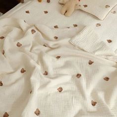 a teddy bear laying on top of a bed with white sheets and pillows next to it