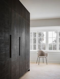 an empty room with a chair next to a large wooden cabinet in the middle of it