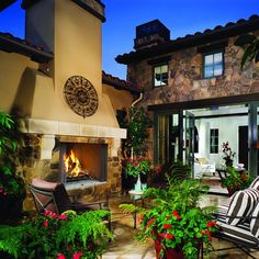 an outdoor patio with chairs and potted plants in front of the fireplace at night