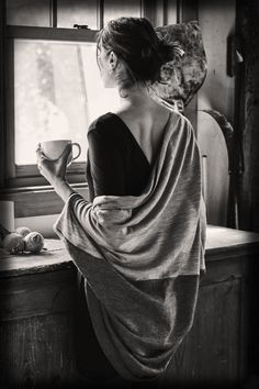 a woman sitting at a window sill holding a cup