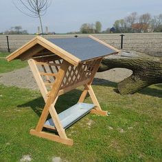 a wooden structure sitting on top of a green grass covered field next to a fallen tree