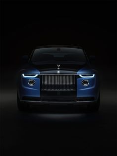 the front end of a blue rolls royce on a black background with its lights on