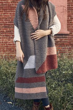 a woman standing in front of a brick wall wearing a gray and pink knitted shawl