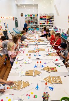 a group of children sitting at a table making gingerbread cutouts on paper