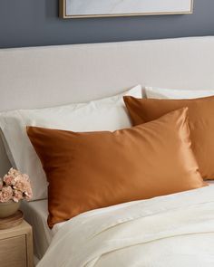 a white bed topped with two pillows and a vase filled with flowers next to it