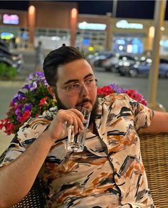 a man sitting on a chair drinking from a wine glass in front of some flowers