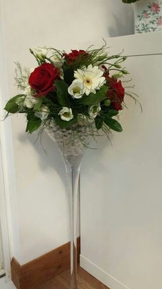 a vase filled with red and white flowers on top of a wooden floor next to a wall