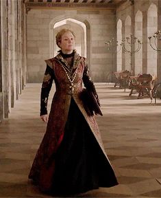 the woman is dressed in medieval clothing and walking through an old building with stone pillars