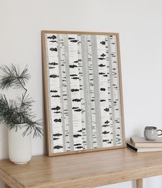 a wooden table topped with a white vase filled with flowers and a framed birch tree print