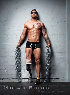 a shirtless man with chains around his ankles and feet, standing in front of a white brick wall