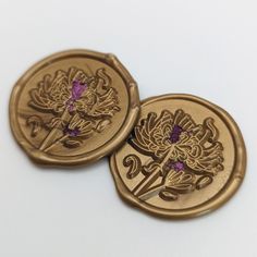 two gold buttons with flowers on them sitting next to each other in front of a white background