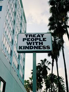 there is a sign that says treat people with kindness in front of some palm trees