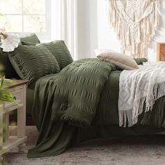 a bed with green comforter and pillows in a white room next to a window