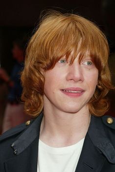 a close up of a person wearing a jacket and smiling at the camera with red hair