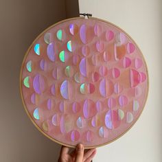 a person holding up a pink and purple artwork piece with circles on it in front of a white wall