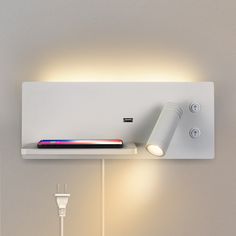 an electronic device is sitting on a shelf next to a wall light and plugged in