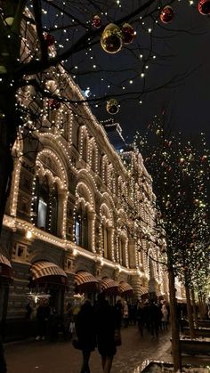 people are walking down the street in front of christmas lights and trees with umbrellas