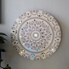 a decorative wall hanging on the side of a white wall next to a potted plant