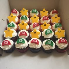 cupcakes with white frosting and red, green and yellow decorations are arranged in a cardboard box