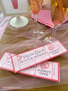 two wine glasses and three tickets on a table with pink napkins in front of them