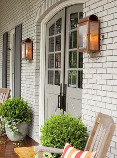 a porch with chairs and potted plants on the front steps, next to an open door