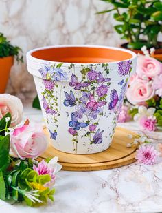 a flower pot sitting on top of a wooden tray next to pink and white flowers