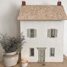 a white doll house sitting on top of a wooden table next to a potted plant