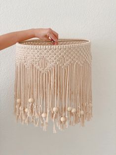 a hand holding a macrame lamp shade with tassels and beads on it