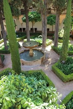 an outdoor fountain surrounded by trees and plants in a courtyard area with stone walkways