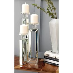 a tall mirrored candle holder with four candles on top of it and a vase next to it