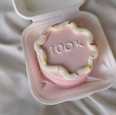 a pink cake in a plastic container with the word 100k written on it