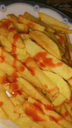 french fries covered in ketchup on a white and blue plate with silverware