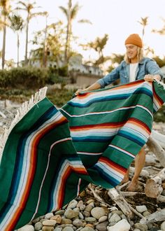 a woman is holding up a blanket on the rocks in front of some palm trees