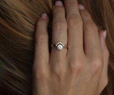 a woman's hand with a diamond ring on her left hand and hair in the background