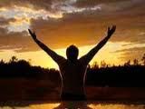 a man is standing in the water with his hands up and arms wide open at sunset