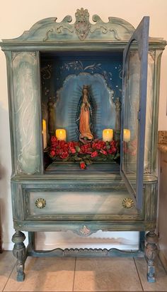 an old blue cabinet with candles and flowers on it in front of a wall mounted statue