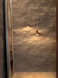 two lights hanging from the ceiling in a room with wood flooring and stone walls