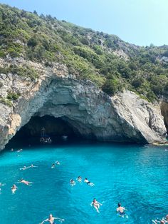 people swimming in the water near a cave