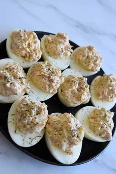 deviled eggs with dill sprinkled on them in a black plate sitting on a marble countertop