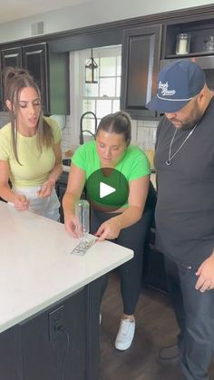 three people standing around a kitchen counter looking at something on the tabletop in front of them