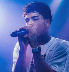 a man with tattoos on his face holding a microphone up to his mouth while standing in front of a blue light