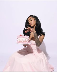 a woman in a pink dress is holding a cake and posing for the camera with her hands