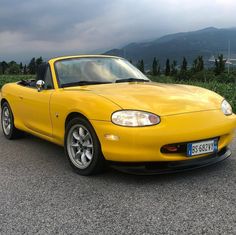 a yellow sports car is parked on the side of the road with mountains in the background