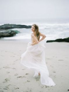 a woman standing on top of a sandy beach next to the ocean wearing a white dress